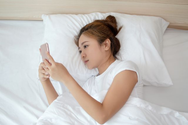 ベッドで携帯を見る女性